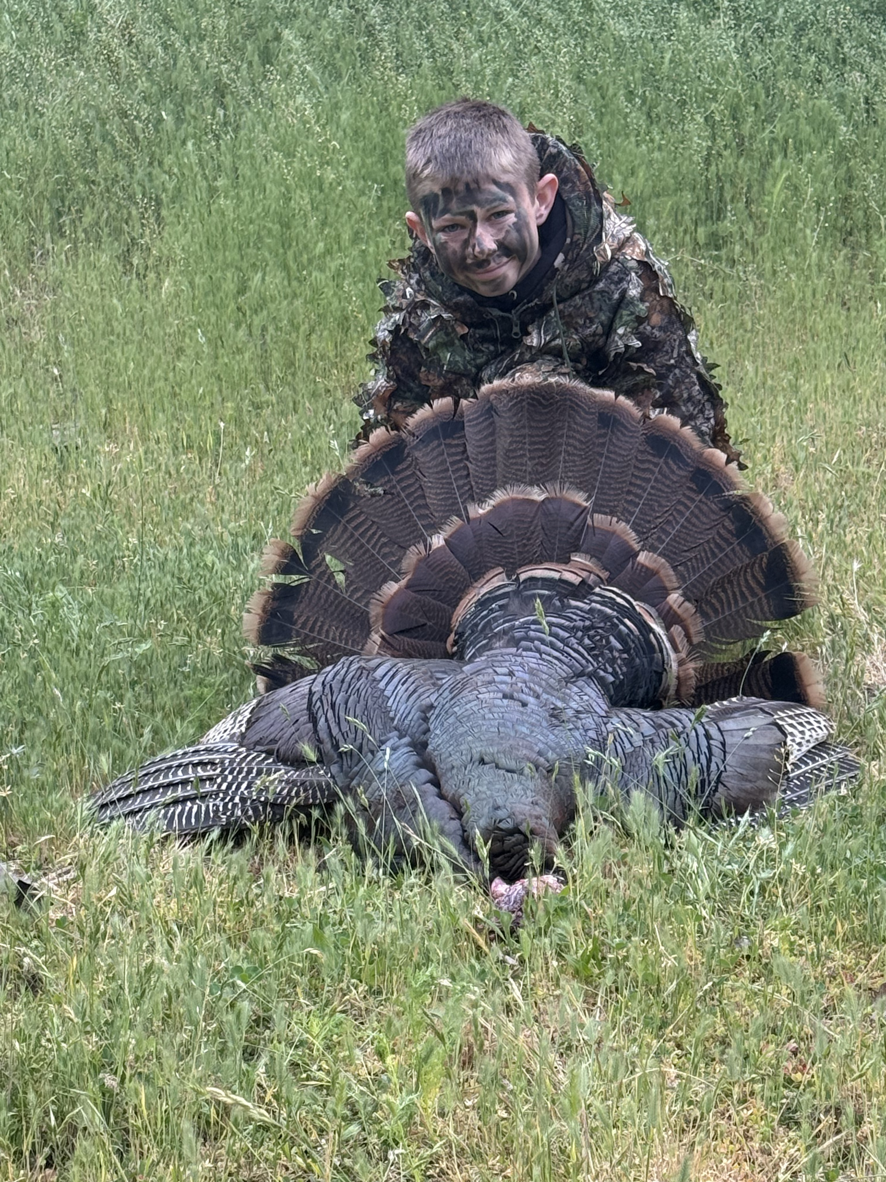 Young hunter with a turkey in a grassy field